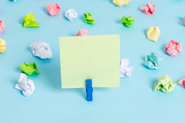 Mavi arka planda boş dikdörtgen kare şeklinde hatırlatma notu etrafında yerleştirilen renkli buruşuk levhalar. Ofis malzemeleri, bir bağlantı elemanı tarafından sabitlenmiş boş kağıt.