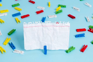 Mavi bir arka plan ortasında boş dikdörtgen kare şeklinde hatırlatma notu etrafında yerleştirilen renkli clothespin. Ofis malzemeleri, bir bağlantı elemanı tarafından sabitlenmiş boş kağıt.