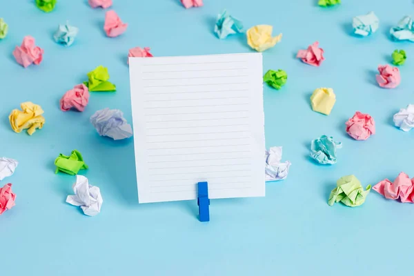 Hojas arrugadas de color colocadas alrededor del rectángulo vacío en forma cuadrada nota recordatorio en el fondo azul. Material de oficina, papel en blanco fijado por un cierre . — Foto de Stock