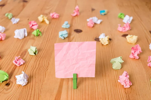 Carte colorate accartocciate intorno a un rettangolo vuoto di forma quadrata nota di richiamo al centro di un pavimento in legno tenuto da una molletta verde. Legno con scanalature. Forniture per ufficio . — Foto Stock