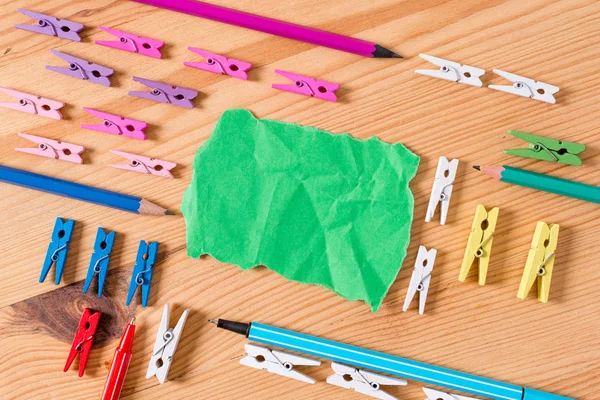 Gekleurde wasknijper geplaatst rond de lege rechthoek vierkant vormige herinnering opmerking in het midden van een houten vloer. Hout met groeven en sleuven. Kantoorbenodigdheden, potlood en pen. — Stockfoto