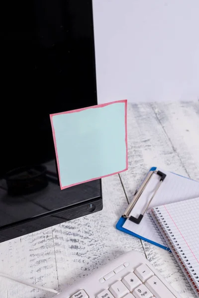 Notacja papier trzymać się czarny ekran komputera w pobliżu białej klawiatury i nieruchomy nad drewnianym stole. Monitor PC umieszczony w pobliżu urządzenia do pisania z niebieskim taśmy notatki na nim. — Zdjęcie stockowe