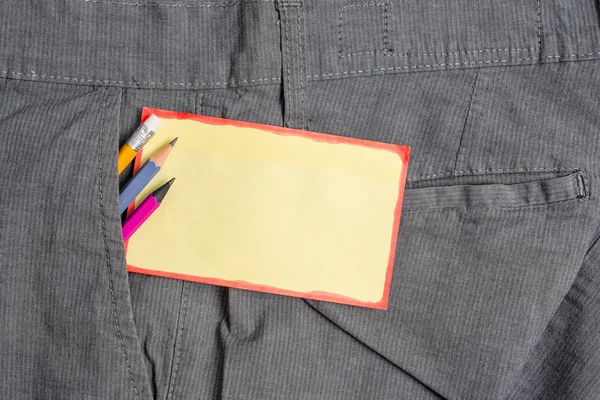 Skriv utrustning och ett gult anteckningspapper inuti den formella arbets byxan framficka. Stationär penna med notationsark placeras i man arbete byxor — Stockfoto