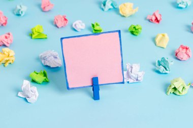 Mavi arka planda boş dikdörtgen kare şeklinde hatırlatma notu etrafında yerleştirilen renkli buruşuk levhalar. Ofis malzemeleri, bir bağlantı elemanı tarafından sabitlenmiş boş kağıt.