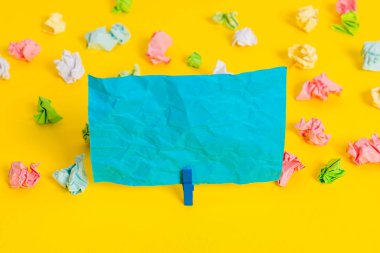 Sarı arkaplandaki boş dikdörtgen kare şekilli hatırlatma notunun etrafına yerleştirilmiş renkli buruşuk çarşaflar. Ofis malzemeleri, boş kağıtlar..