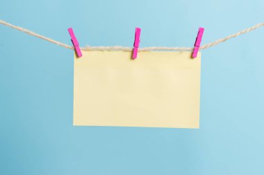 Dikdörtgen şeklinde not renkli kağıt beyaz ahşap arka planda clothespin tarafından bir çamaşır ipi kırpılmış. Kare boş hatırlatma ve ofis ekipmanları malzemeleri hafif ahşap bir masada.