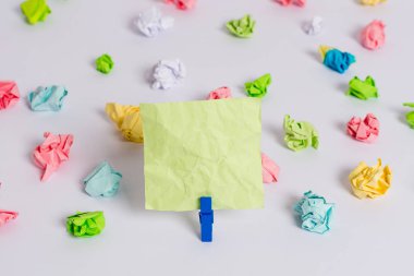 Beyaz bir zeminin ortasında boş dikdörtgen kare şeklinde hatırlatma notu etrafında yerleştirilen renkli buruşuk levhalar. Ofis malzemeleri, bir bağlantı elemanı tarafından sabitlenmiş boş kağıt.