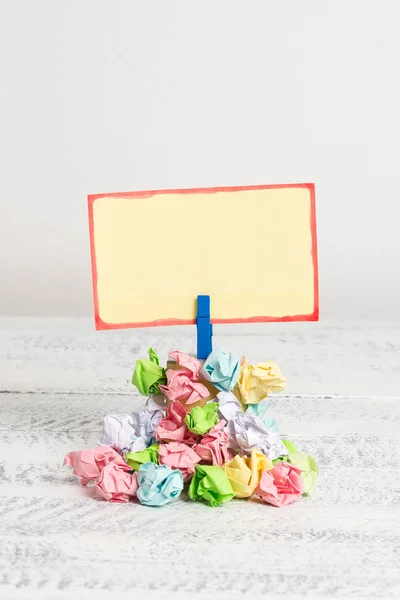 Rappel carré au-dessus d'une pile de papiers froissés fixés par une pince à linge bleue. Différentes feuilles empilées sous une note colorée vide. Sol en bois blanc et fond blanc . — Photo