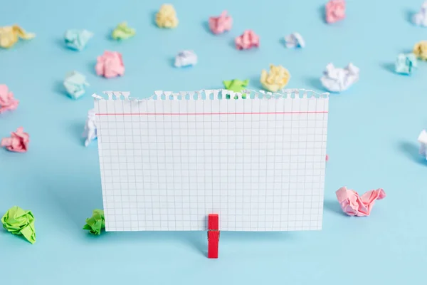 Papeles arrugados coloridos y rectángulo cuadrado en forma de nota de color en un fondo azul. Clip rojo colgando un papel recordatorio en un espacio en blanco. Mesa de oficina ligera . — Foto de Stock