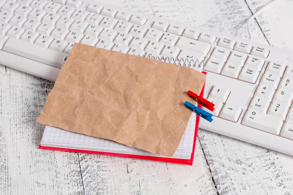 Vierkante papieren notitieboekje met een rechthoek vormige lege notitie boven vastgemaakt door twee wasknijpers op het blad. Wit toetsenbord onder een beurt en lichte houten vloer achtergrond. — Stockfoto