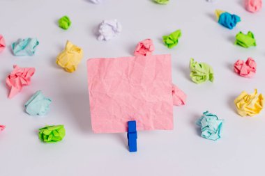 Beyaz bir zeminin ortasında boş dikdörtgen kare şeklinde hatırlatma notu etrafında yerleştirilen renkli buruşuk levhalar. Ofis malzemeleri, bir bağlantı elemanı tarafından sabitlenmiş boş kağıt.