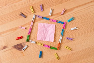 Renkli clothespin kare şeklinde yerleştirilir ve ahşap bir zemin ortasında boş bir dikdörtgen hatırlatma notu işaret. Oluklar ve yuvaları ile ahşap. Ofis malzemeleri.