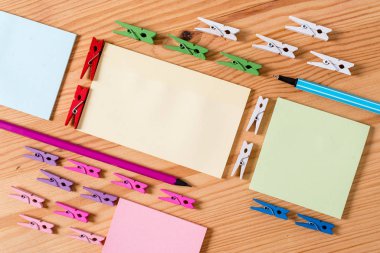 Ahşap bir zeminin ortasında boş dikdörtgen kare şeklinde hatırlatma notu etrafında yerleştirilen renkli clothespin. Oluklar ve yuvaları ile ahşap. Ofis malzemeleri, kalem ve kalem.