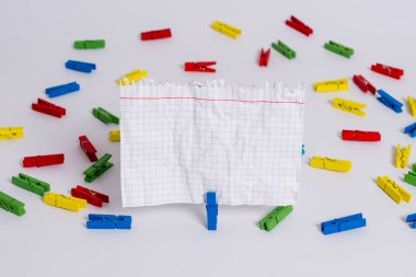 Beyaz bir zeminin ortasında boş dikdörtgen kare şeklinde hatırlatma notu etrafında yerleştirilen renkli clothespin. Ofis malzemeleri, bir bağlantı elemanı tarafından sabitlenmiş boş kağıt.