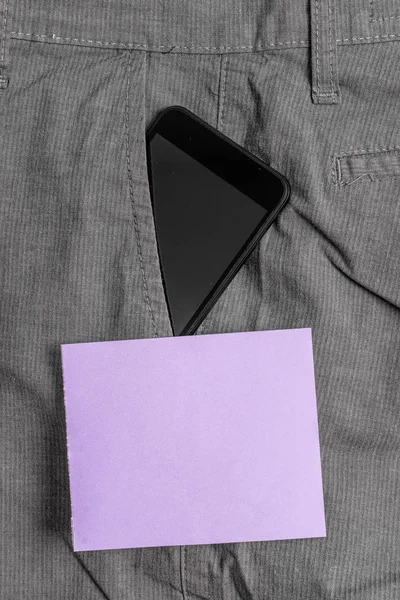 Mor bir not kağıt yakınında resmi çalışma pantolon ön cebinde siyah akıllı telefon cihazı. Modern gadget notasyon levha yakın erkek pantolon içine yerleştirilir — Stok fotoğraf