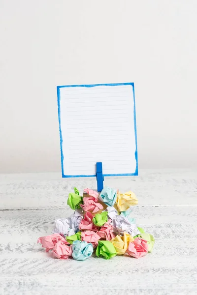 Rappel carré au-dessus d'une pile de papiers froissés fixés par une pince à linge bleue. Différentes feuilles empilées sous une note colorée vide. Sol en bois blanc et fond blanc . — Photo