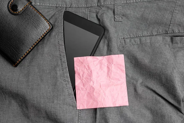 Smartphone készülék a nadrág elülső zsebében egy pénztárca és rózsaszín jegyzet papír. Korszerű szerkentyű van elhelyezett belső rész ember nadrág mellett jelölés lepedő plusz pénztárca — Stock Fotó