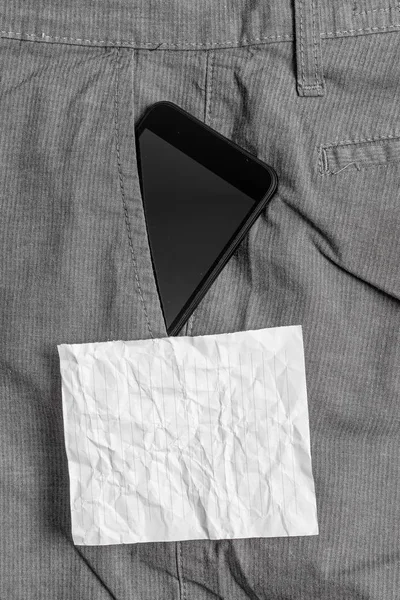 Svart smartphone-enhet i den formella arbets byxorna framficka nära ett vitt anteckningspapper. Modern gadget är placerad inuti man Pants nära notationsark — Stockfoto