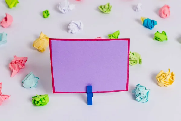 Folhas de crumpled coloridas colocadas em torno da nota de lembrete em forma quadrada retangular vazia no centro de um piso branco. Material de escritório, papel em branco fixado por um fixador . — Fotografia de Stock