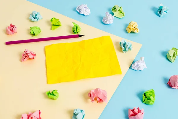 Folhas de crumpled coloridas e um lápis colocado em torno da nota de lembrete em forma de retângulo vazio no centro de um fundo azul e quadrado amarelo. Material de escritório, fixador . — Fotografia de Stock