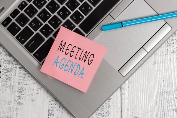 Conceptual hand writing showing Meeting Agenda. Business photo text items that participants hope to accomplish at a meeting Open slim metallic laptop blank sticky pad pen lying vintage table.