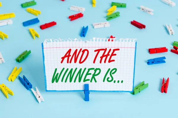 Text sign showing And The Winner Is. Conceptual photo announcing a demonstrating or thing that wins something Colored clothespin papers empty reminder blue floor background office pin. — Stock Photo, Image
