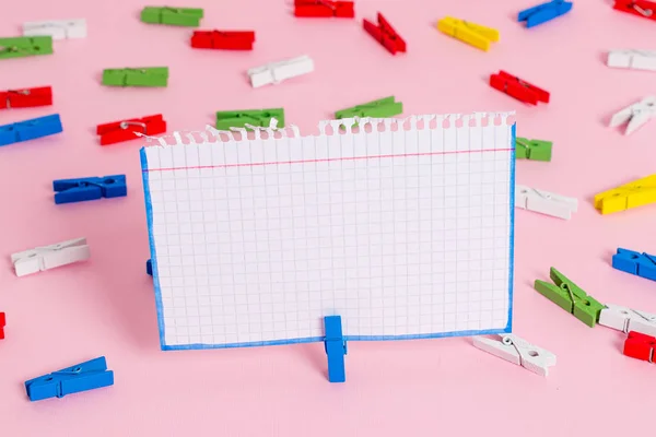 Gekleurde wasknijper geplaatst rond de lege rechthoek vierkant vormige herinnering notitie in het midden van een roze achtergrond. Kantoorbenodigdheden, blanco papier vastgemaakt door een bevestiger. — Stockfoto