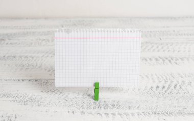 Yeşil clothespin beyaz ahşap arka plan içinde dikdörtgen kare şeklinde renkli kağıt tutan. Kliple sabitlenmiş boş bir alanda renkli not anımsatıcı.