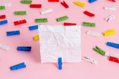 Pembe bir arka plan ortasında boş dikdörtgen kare şeklinde hatırlatma notu etrafında yerleştirilen renkli clothespin. Ofis malzemeleri, bir bağlantı elemanı tarafından sabitlenmiş boş kağıt.