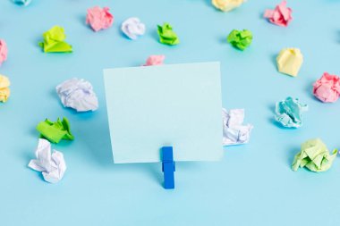 Mavi arka planda boş dikdörtgen kare şeklinde hatırlatma notu etrafında yerleştirilen renkli buruşuk levhalar. Ofis malzemeleri, bir bağlantı elemanı tarafından sabitlenmiş boş kağıt.