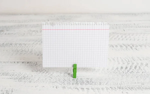 Green clothespin holding a rectangle square shaped colored paper in a white wood background. Colorful note reminder in a blank space pinned by a clip. — Stock Photo, Image