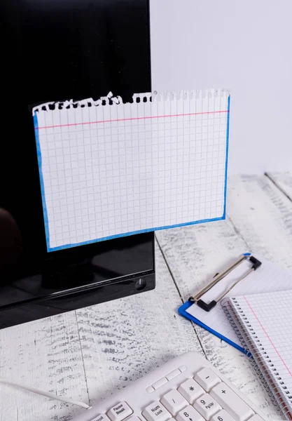 Notatie papier stick naar zwart computerscherm in de buurt van witte toetsenbord en stationair boven de houten tafel. PC-monitor geplaatst in de buurt van schrijf apparatuur met witte notitie blad tape erop. — Stockfoto