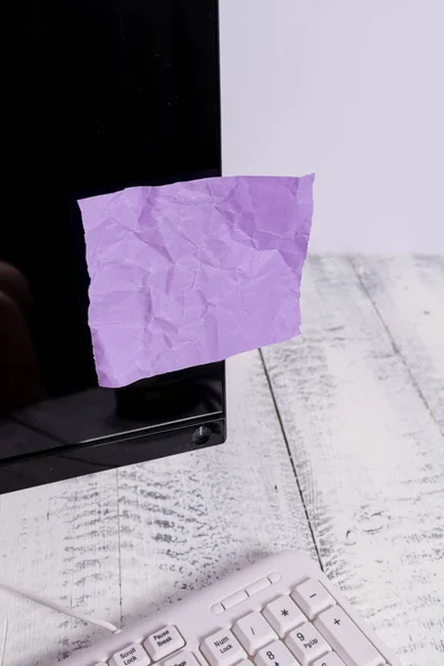 表記用紙は、木製のテーブルの上の白いキーボードの近くに黒いコンピュータの画面に貼り付けます。紫色のノートシートがテープで留められたqwertyの近くに置かれたPCモニター. — ストック写真