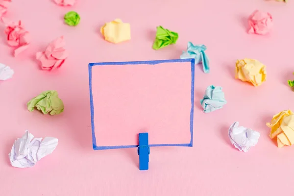 Folhas de crumpled coloridas colocadas em torno da nota de lembrete em forma quadrada retangular vazia no fundo rosa. Material de escritório, papel em branco fixado por um fixador . — Fotografia de Stock