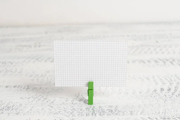 Espinha de roupa verde segurando um retângulo quadrado em forma de papel colorido em um fundo de madeira branca. Lembrete de nota colorida em um espaço em branco fixado por um clipe . — Fotografia de Stock