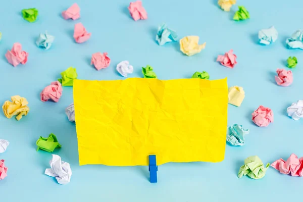 Hojas arrugadas de color colocadas alrededor del rectángulo vacío en forma cuadrada nota recordatorio en el fondo azul. Material de oficina, papel en blanco fijado por un cierre . — Foto de Stock