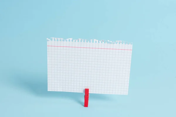 Pince à linge colorée et rectangle en forme de carré papier coloré dans un fond bleu. Clip rouge accrochant un rappel de note dans un espace vide. Table de bureau légère avec papiers . — Photo