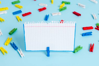 Mavi bir arka plan ortasında boş dikdörtgen kare şeklinde hatırlatma notu etrafında yerleştirilen renkli clothespin. Ofis malzemeleri, bir bağlantı elemanı tarafından sabitlenmiş boş kağıt.