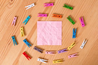 Renkli clothespin ahşap bir zemin ortasında boş bir dikdörtgen kare şeklinde hatırlatma notu etrafında daireler halinde yayıldı. Oluklar ve yuvaları ile ahşap. Ofis malzemeleri.