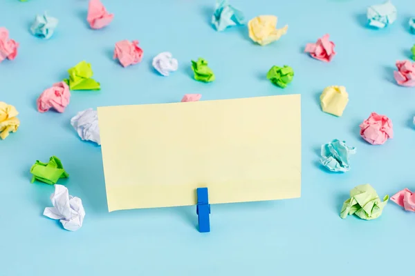 Hojas arrugadas de color colocadas alrededor del rectángulo vacío en forma cuadrada nota recordatorio en el fondo azul. Material de oficina, papel en blanco fijado por un cierre . — Foto de Stock