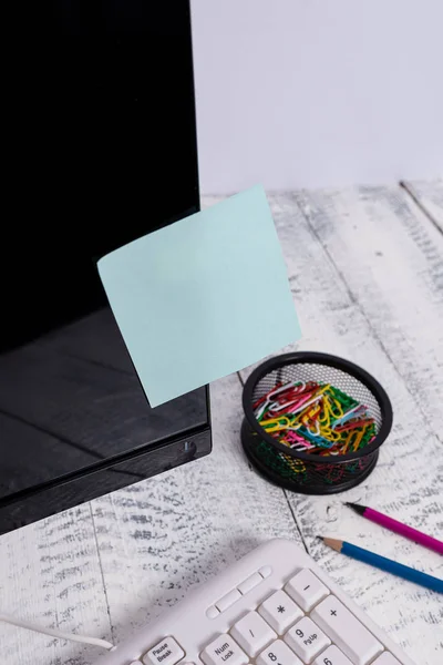 El papel de la notación se pega a la pantalla negra del ordenador cerca del teclado blanco y estacionario sobre la mesa de madera. Monitor de PC colocado cerca del equipo de escritura con cinta de hoja de nota azul . — Foto de Stock