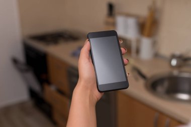 Genç bayan evin içinde karanlık bir akıllı telefon kullanıyor. Evin ambiyansında siyah bir cep telefonu tutan kadın. Boş alan ile teknolojik cihazlar ve ofis malzemeleri ile Kız.