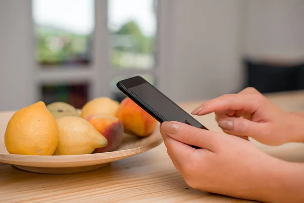 Ung dam med en mörk smartphone i hemmet. Kvinna som håller en svart mobiltelefon i ett hus ambient. Flicka med tekniska enheter och kontorsmateriel med tomt utrymme. — Stockfoto