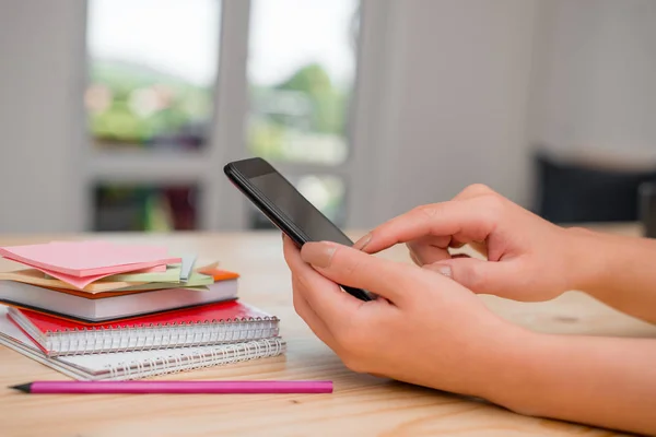 Jovencita usando un teléfono inteligente oscuro dentro de casa. Mujer sosteniendo un celular negro en el ambiente de una casa. Chica con dispositivos tecnológicos y suministros de oficina con espacio en blanco . — Foto de Stock