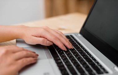 Genç bayan gri bir dizüstü bilgisayar kullanarak ve arka planda kahve veya çay bir fincan ile siyah klavye yazarak. Ofis malzemeleri, teknolojik cihazlar ve ahşap masa.