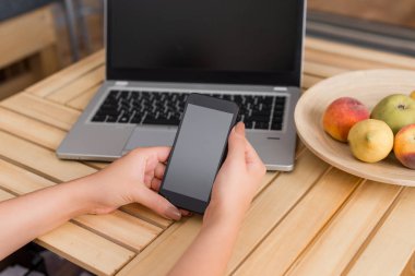 Genç bayan kullanarak ve siyah kahve bir fincan ile bir sandık masada karanlık bir akıllı telefon tutarak. Ofis malzemeleri, cep telefonu, teknolojik cihazlar ve ahşap masa.