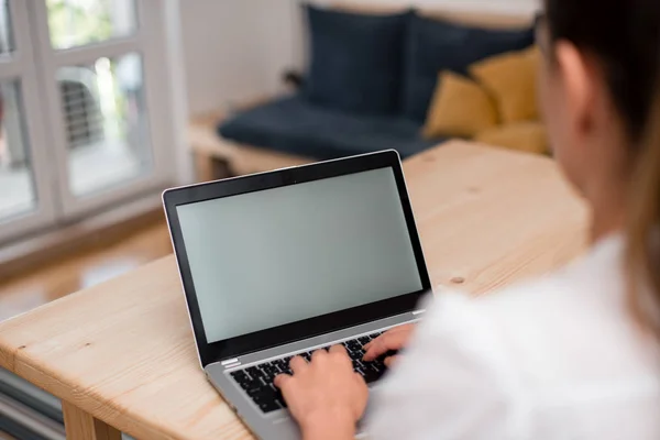 Jonge dame met behulp van een grijze laptop computer en het typen van het zwarte toetsenbord met beide handen in een kamer. Vrouw in een huis ambient met kantoorbenodigdheden en technologische apparaten. — Stockfoto