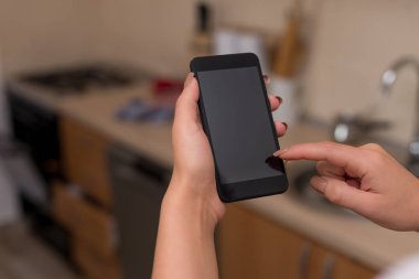 Genç bayan evin içinde karanlık bir akıllı telefon kullanıyor. Evin ambiyansında siyah bir cep telefonu tutan kadın. Boş alan ile teknolojik cihazlar ve ofis malzemeleri ile Kız.