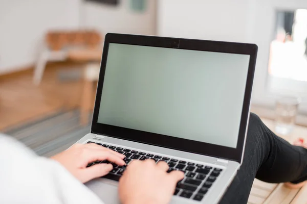Молода леді використовує сірий ноутбук і друкує в чорній клавіатурі з обома руками в кімнаті. Жінка в будинку з офісними приладдям і технологічними пристроями . — стокове фото