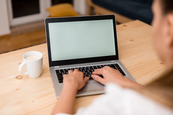 Молодая леди, используя серый ноутбук и печатая на черной клавиатуре с кружкой кофе или чая на заднем плане. Офисные принадлежности, технологические приборы и деревянный стол . — стоковое фото
